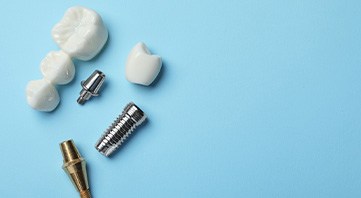 Dental implant posts, abutment, bridge, and crown on light blue surface