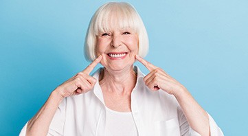 Woman with short white hair pointing to her smile with both hands