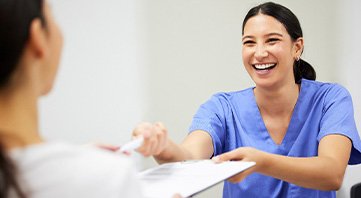 Woman in blue scrubs receiving pen and paperwork from patient