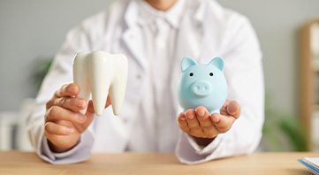 Man in white coat holding piggy bank in one hand and model tooth in the other