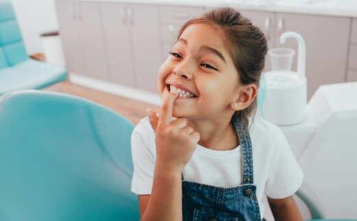 Child pointing to smile during dental checkup and teeth cleaning visit