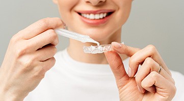 Nose-to-chest view of woman in white shirt applying whitening gel to applicator tray